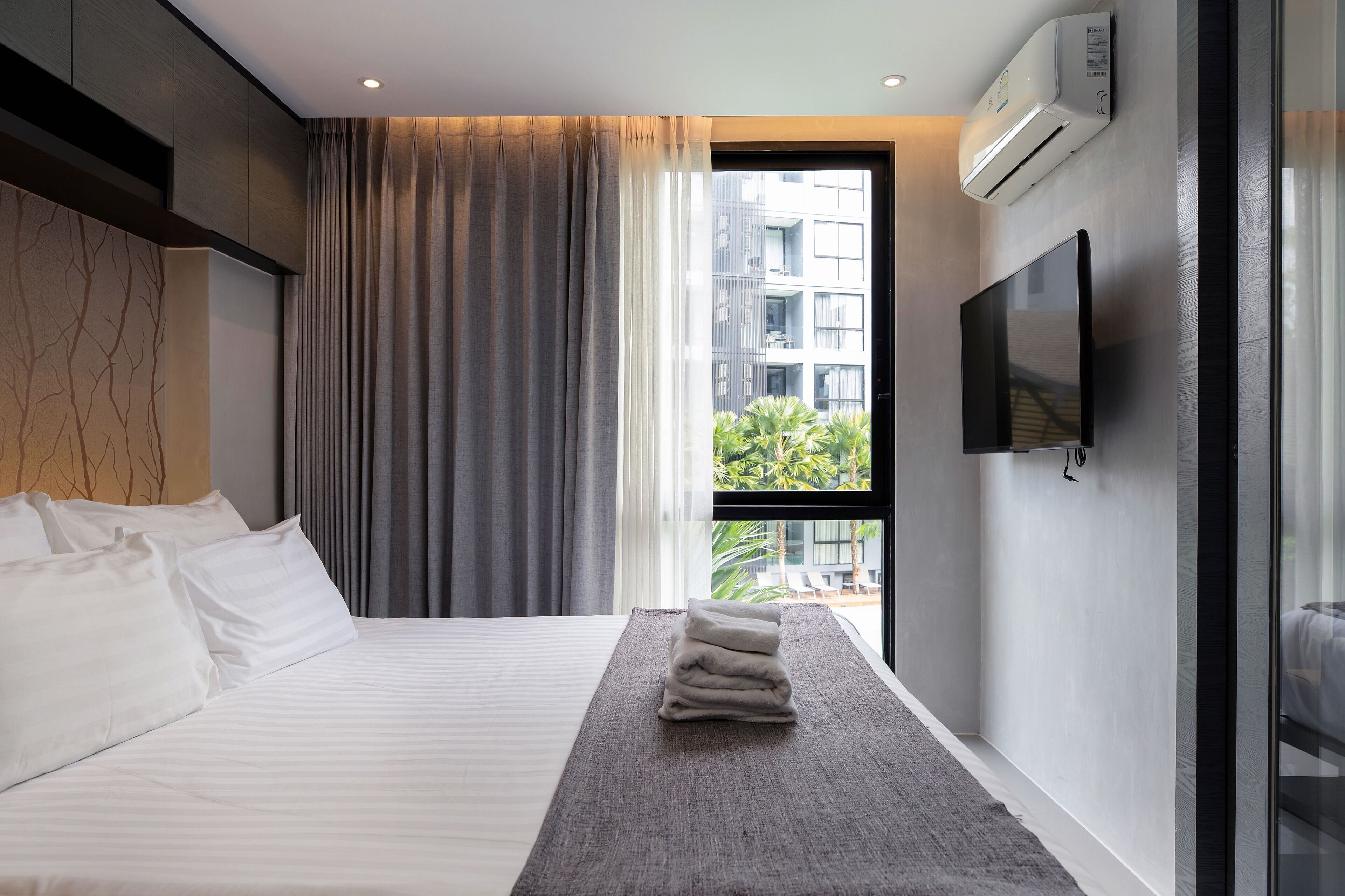 Habitación de hotel moderna con una cama grande, un televisor de pantalla plana y vistas de la ciudad a través de un amplio ventanal.