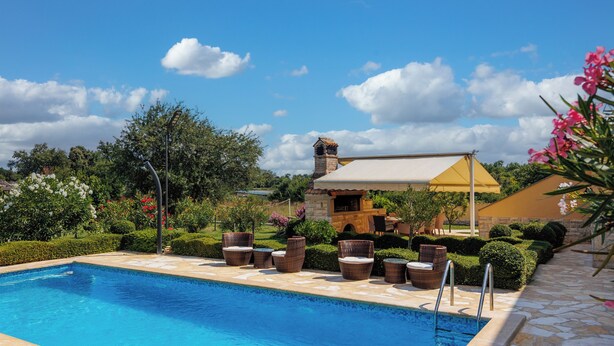 Une piscine entourée de chaises en osier et d’une terrasse en pierre.
