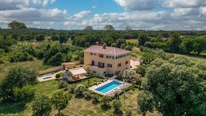 Une grande maison avec une piscine, entourée d’une végétation luxuriante et d’arbres.