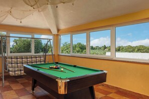 Une table de billard avec des billes, un banc et de grandes fenêtres donnant sur un beau paysage.
