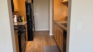 A narrow kitchen with wooden cabinets, a black refrigerator, and a countertop with a sink.