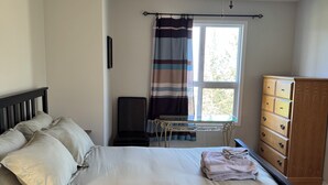 A bedroom with a bed, a ceiling fan, a window with curtains, a dresser, and a desk with a chair.