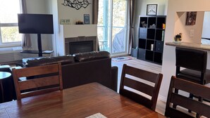 A living room with a wooden dining table, chairs, a fireplace, a TV, and a sliding glass door to the outdoors.