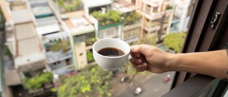 A hand holding a white cup of coffee, with a view of a residential area through a window.