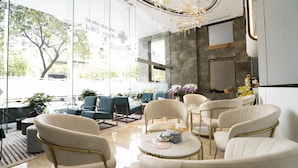 Een moderne hotel lobby met zithoeken, grote ramen en een decoratieve kroonluchter.