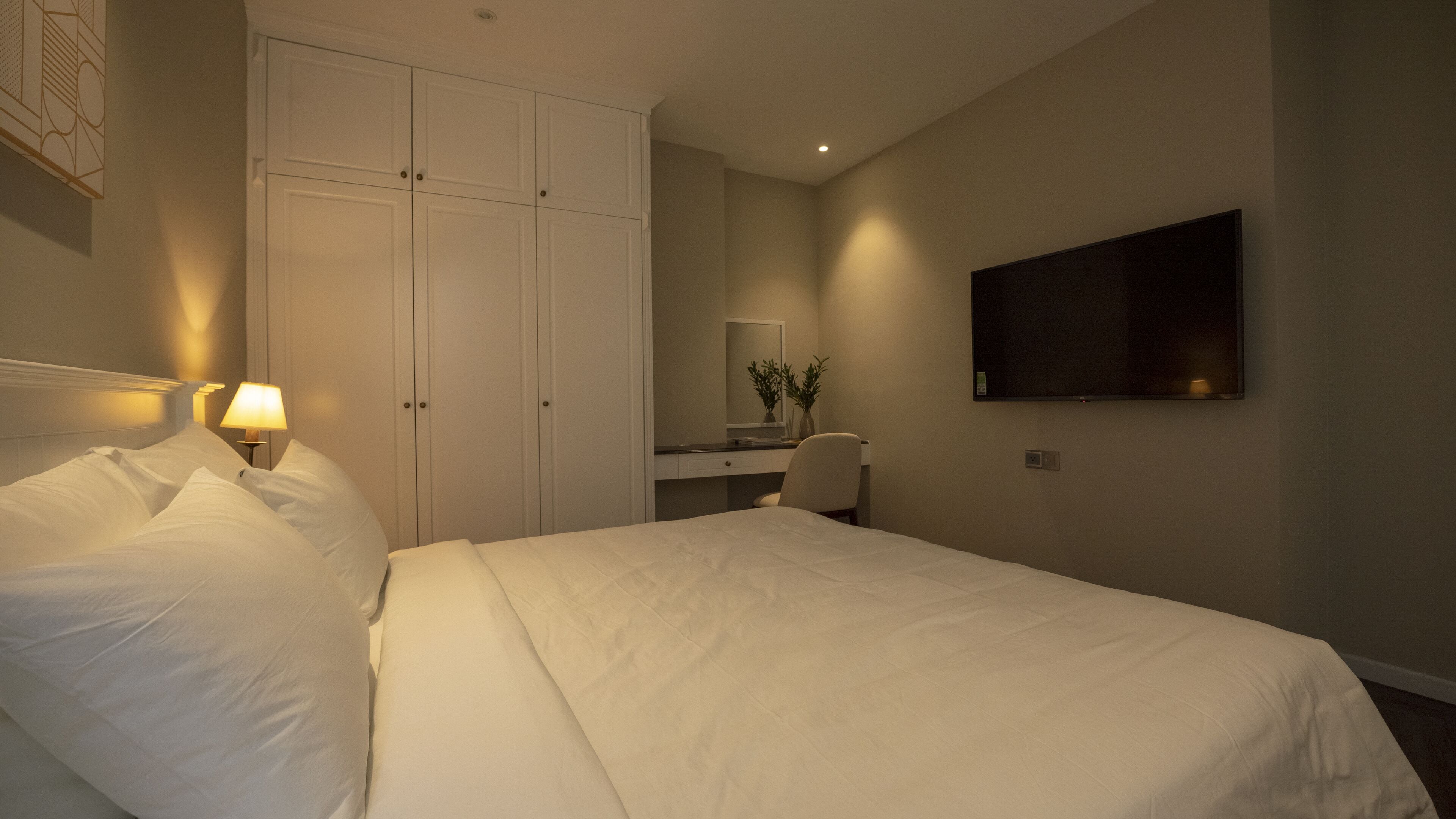 A hotel room with a bed, a desk, a chair, a TV, and a wardrobe.
