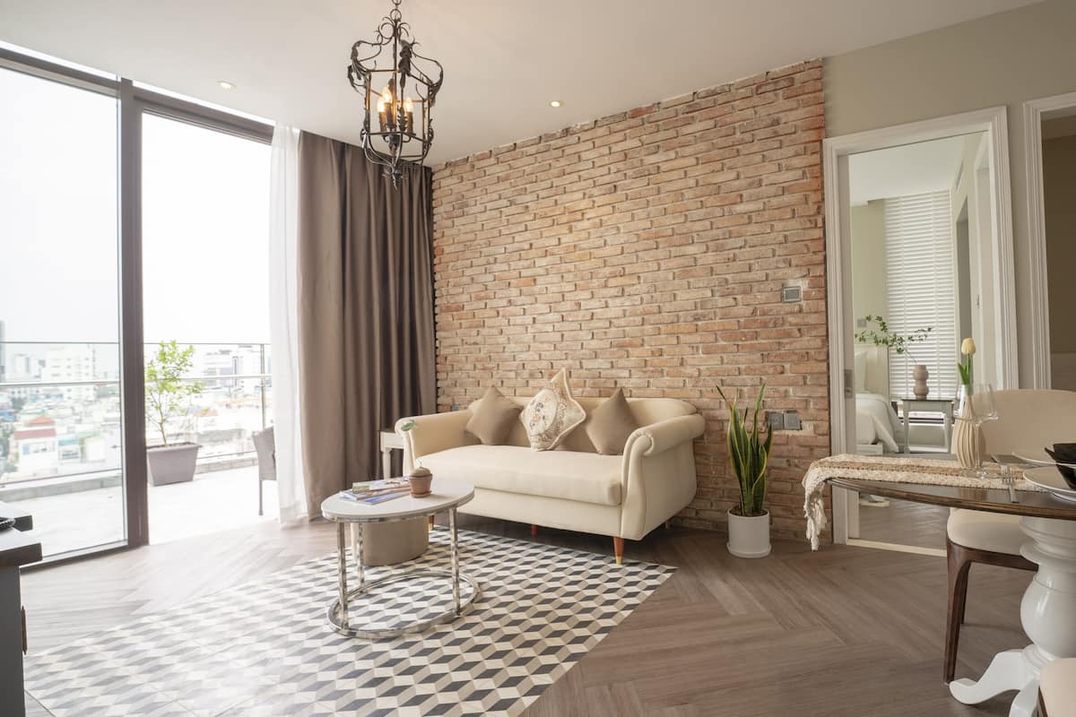 Ein modernes Wohnzimmer mit Backsteinwand, einer Couch, einem Couchtisch und einem Essbereich mit Tisch für zwei Personen.
