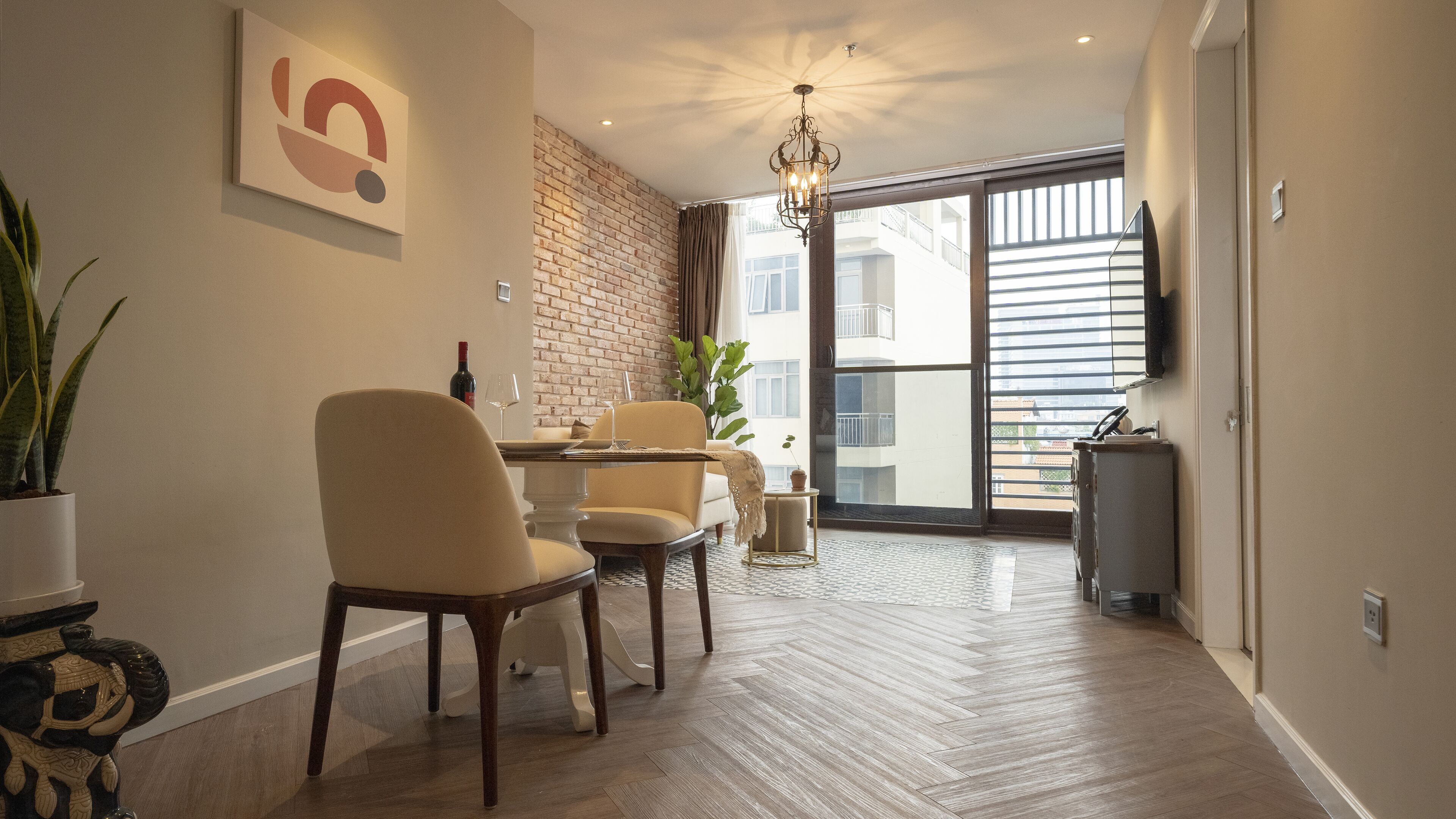 A modern dining area with a brick accent wall, a chandelier, and a view of the city through large windows.