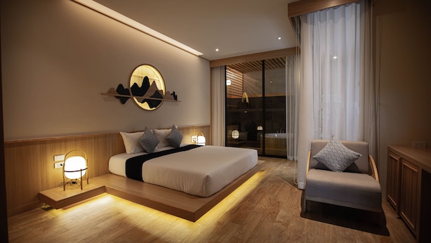 Una habitación de hotel moderna con una cama grande, un área de descanso y vistas a la ciudad a través de la ventana.
