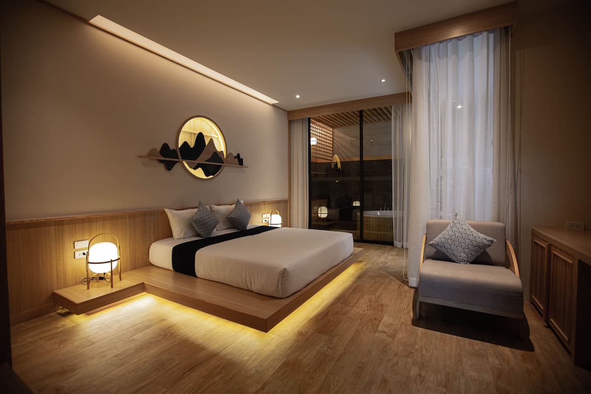 A modern hotel room with a large bed, a seating area, and a view of the cityscape through the window.