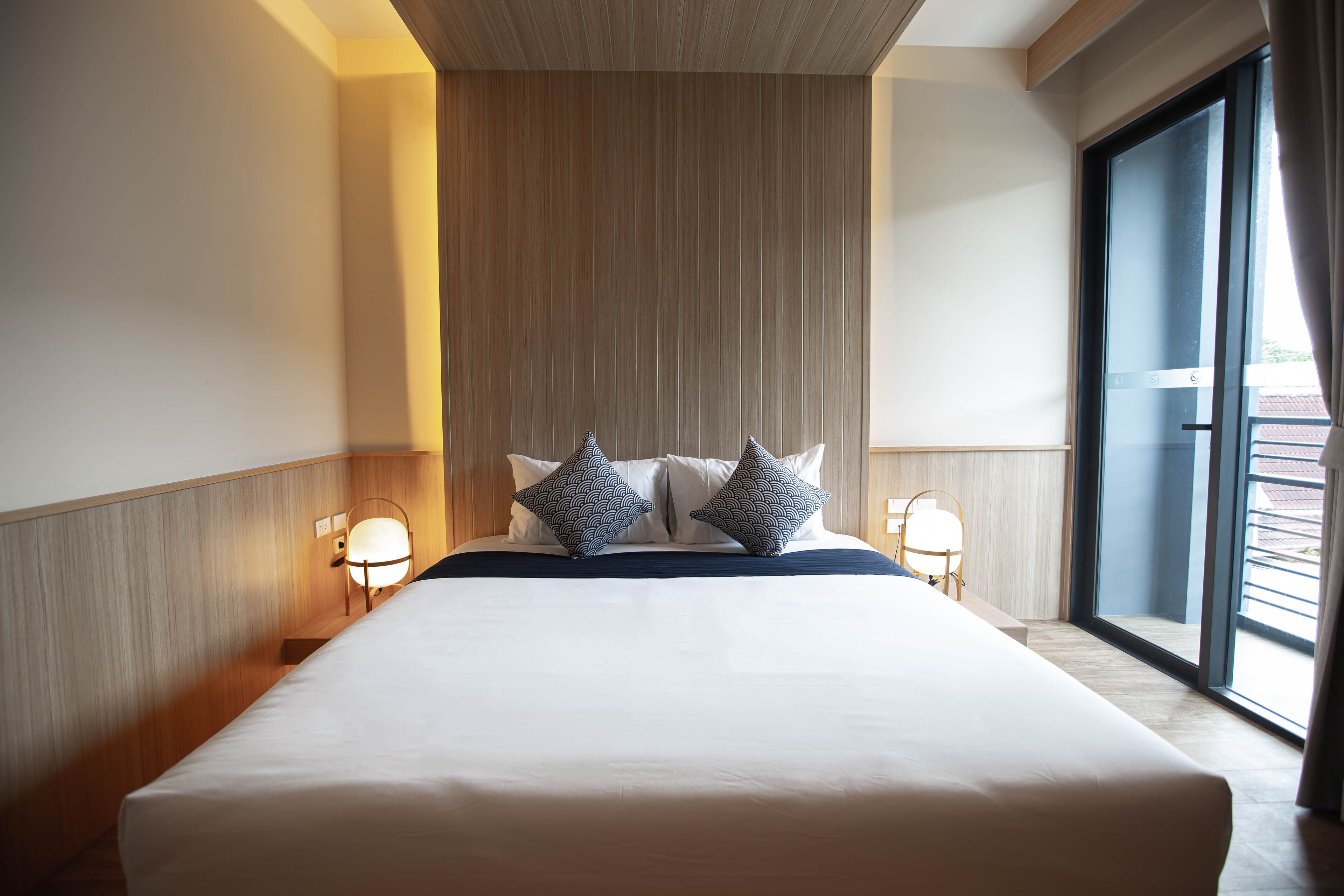 Quarto de hotel com uma cama grande, duas luminárias de cabeceira e vista através de uma janela ampla.