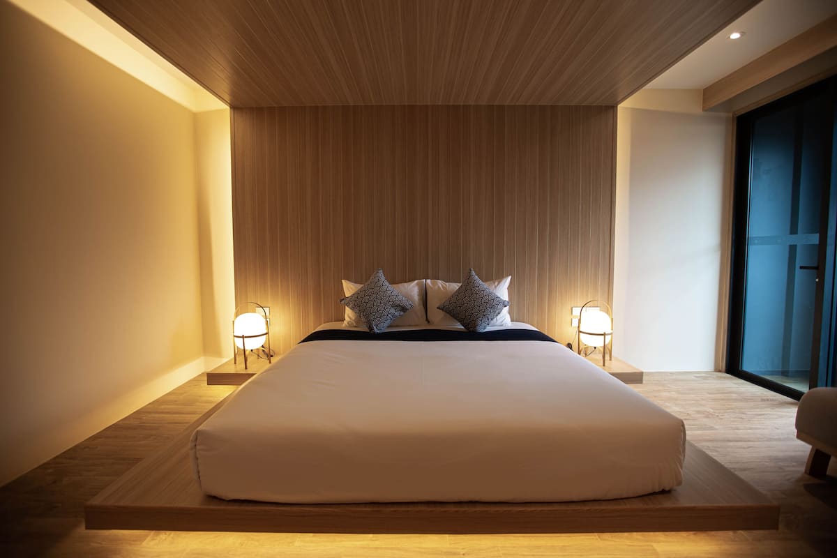 A modern hotel room with a large bed, wooden headboard, and two bedside lamps.
