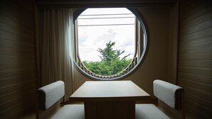 Una habitación pequeña con un ventanal redondo, dos bancos de madera y una mesa.