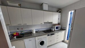Una cocina compacta con armarios blancos, lavadora, microondas y un lavabo.