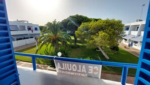 Un balcón con vista a un jardín cuidado, una palmera y un letrero que dice 'CE ALQUILA'.