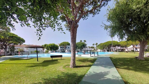 Zona de piscina con sendero empedrado, un banco y árboles.