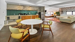 A modern living room with a round white table, yellow chairs, a sofa, and a kitchen area with a green backsplash and wooden shelves. - Berawa Factory Upstairs (Canggu)