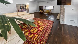 A modern living room with a white sofa, a patterned rug, and a dining area with a table and chairs. - Berawa Factory Upstairs (Canggu)