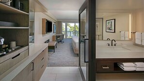 Ein modernes Hotelzimmer mit einem großen Bett, einem Schreibtisch, einem Stuhl, einem Fernseher und einem Badezimmer mit Waschbecken und Handtuchhalter.