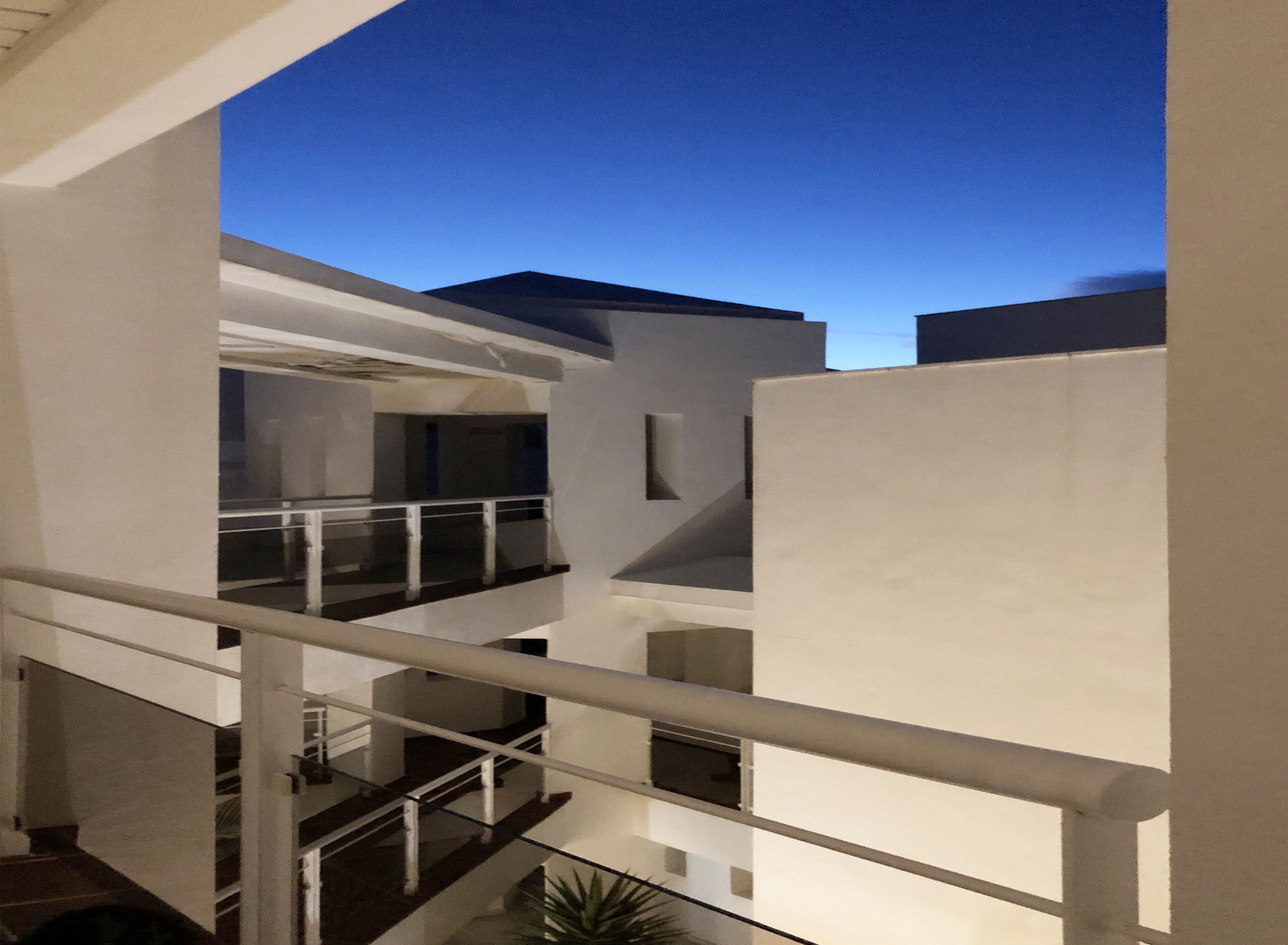 A multi-level building with a glass railing on the upper floor, a staircase, and a view of the sky.