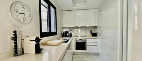 A modern kitchen with white cabinets, a clock, and a window.