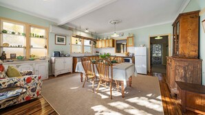 A cozy kitchen with a dining area, wooden cabinets, a refrigerator, and a vintage cabinet. - Secret Garden Cottage (Katoomba)
