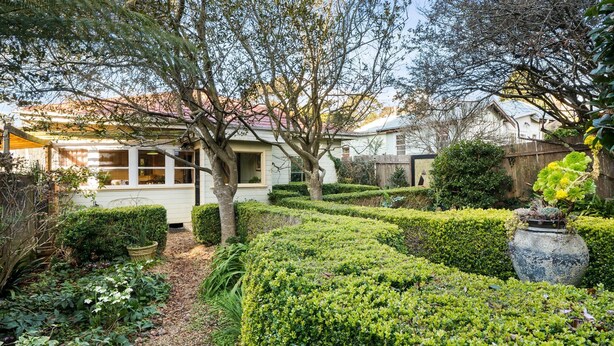 A well-maintained garden with a pathway leading to a house with large windows. - Secret Garden Cottage (Katoomba)