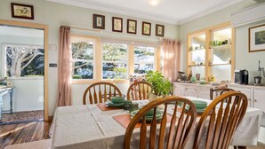 A dining area with a table set for four, wooden chairs, and a view of the garden through large windows. - Secret Garden Cottage (Katoomba)