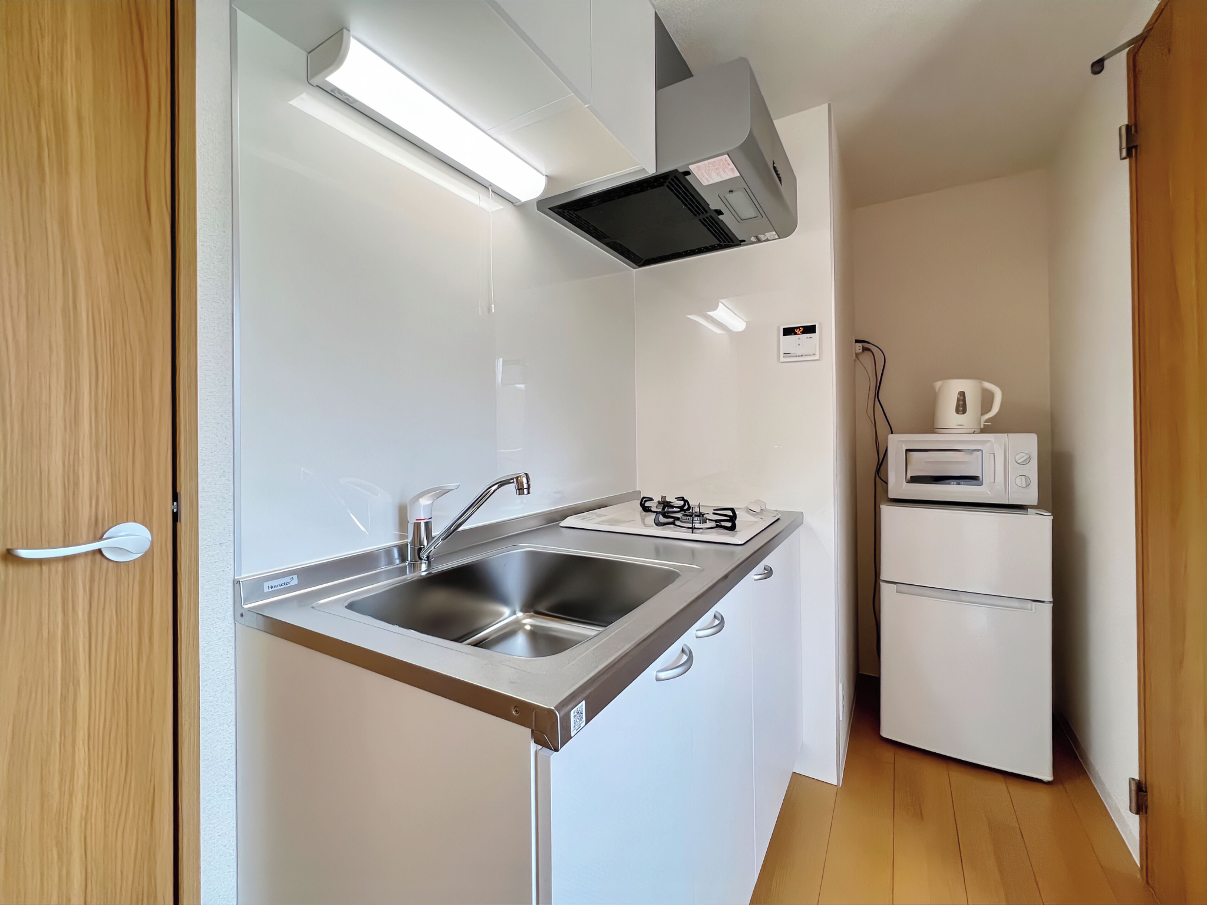 A compact kitchen with a stainless steel sink, a gas stove, a microwave, and a kettle.