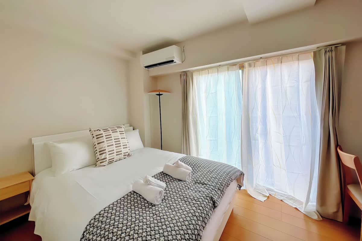 Une chambre d’hôtel avec un lit, une lampe sur pied et une fenêtre avec des rideaux.
