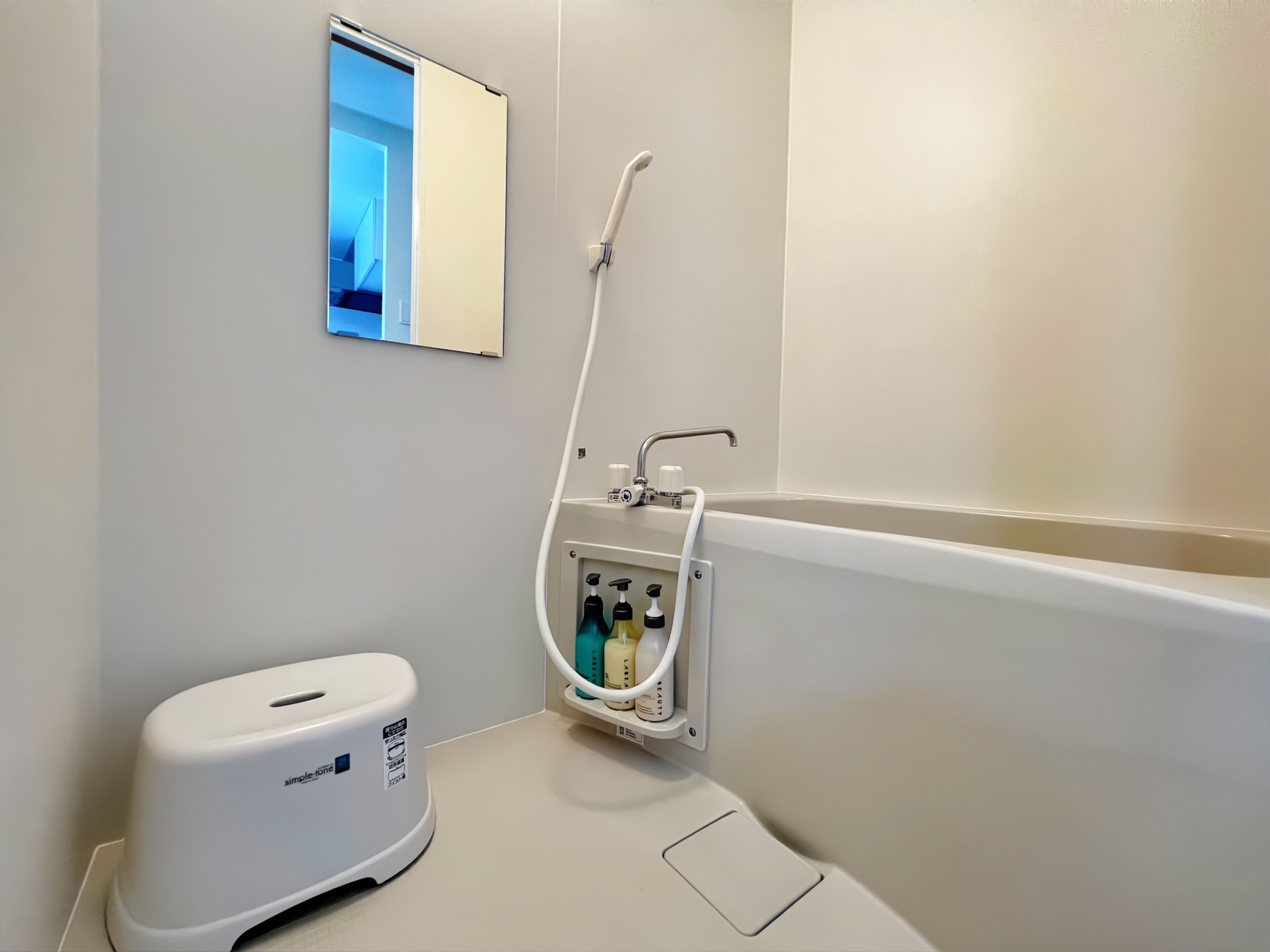A bathroom with a bathtub, a hand soap dispenser, and a mirror.