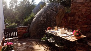 An outdoor dining area with a stone wall, a large rock, and a table set for two with chairs. - Chic Villa Antonina num2178 (Marinella)