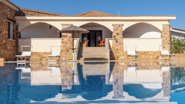 A poolside area with a clear view of a building with stone pillars and a tiled roof. - Chic Villa Antonina 2181 (Marinella)