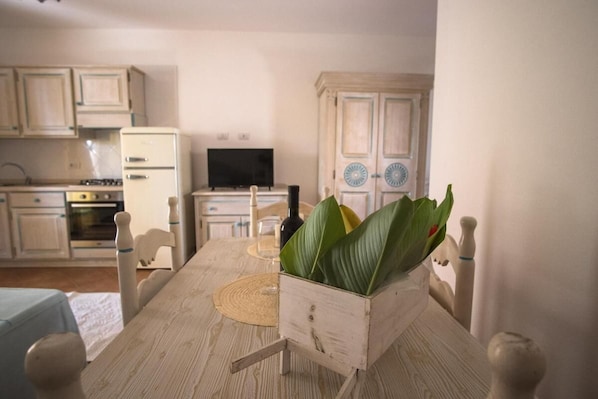 A dining table with chairs, a television, and a kitchen in the background.