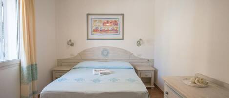 A bedroom with a bed, bedside tables, a dresser, a window with curtains, a hanging light fixture, and a framed picture on the wall.