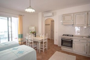 A room with a bed, a dining table with chairs, a kitchen area with cabinets, and a balcony with a view.