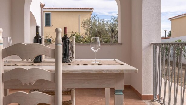 Una mesa con botellas de vino y copas, vista de un edificio y barandilla de balcón.