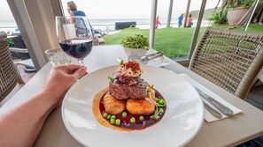 A dining table with a plate of food, a glass of red wine, and a view of the ocean. - 13 Waterside Court, Noosa Waters (Noosaville)