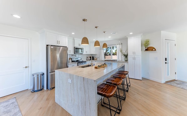 A modern kitchen with white cabinets, stainless steel appliances, a large island with stools, and pendant lighting.