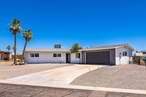 A single-story house with a garage, a driveway, and palm trees.