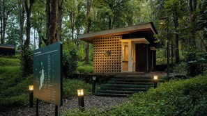 A small, modern building with a wooden lattice facade, surrounded by dense forest.