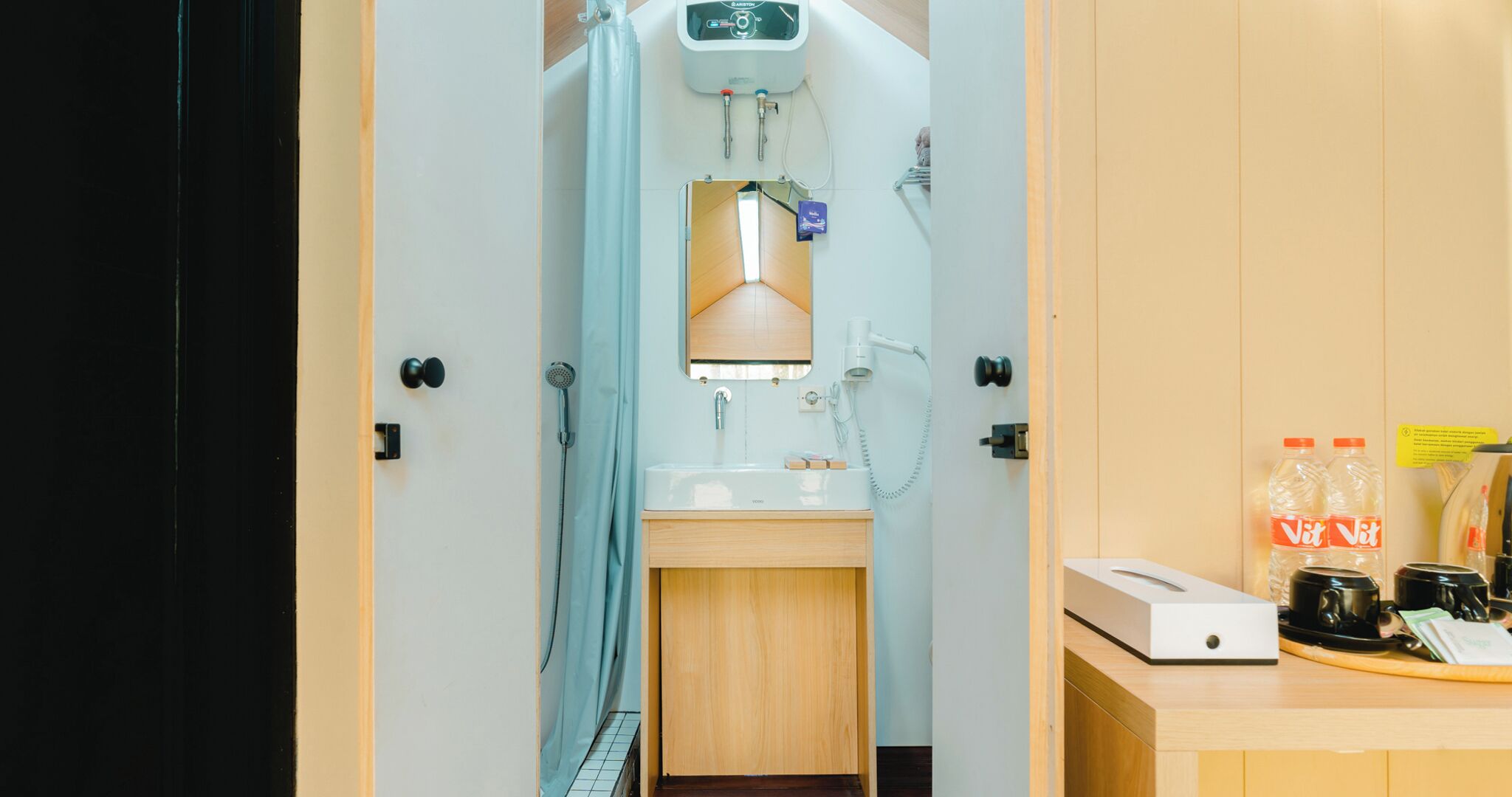 A compact bathroom with a shower, a sink, and a toilet. There is a control panel above the shower, and a small cabinet below the sink.