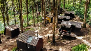 Una zona boscosa amb diverses petites cabanes de color fosc i sostres inclinats, envoltades d'arbres i un camí de terra.
