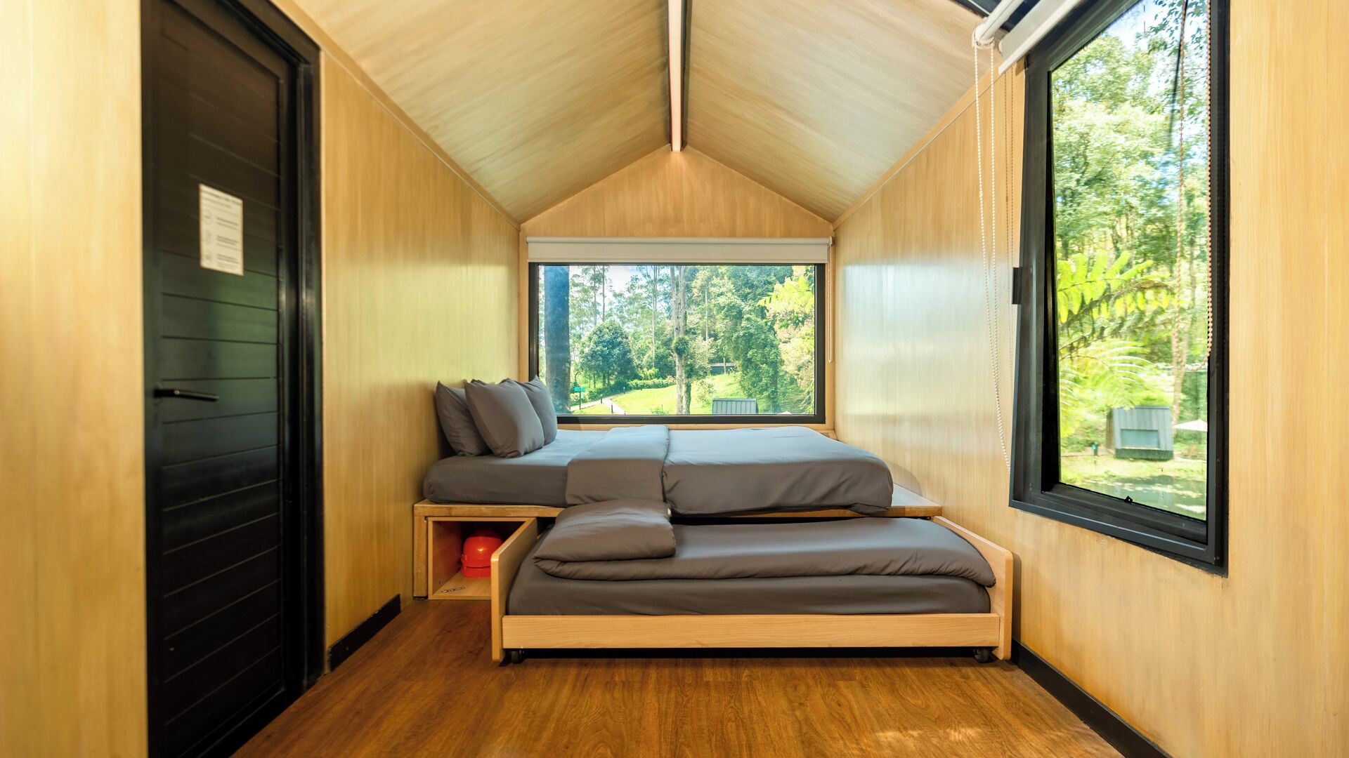 A compact bedroom with a loft bed, a window with a view of greenery, and a door with a sign.