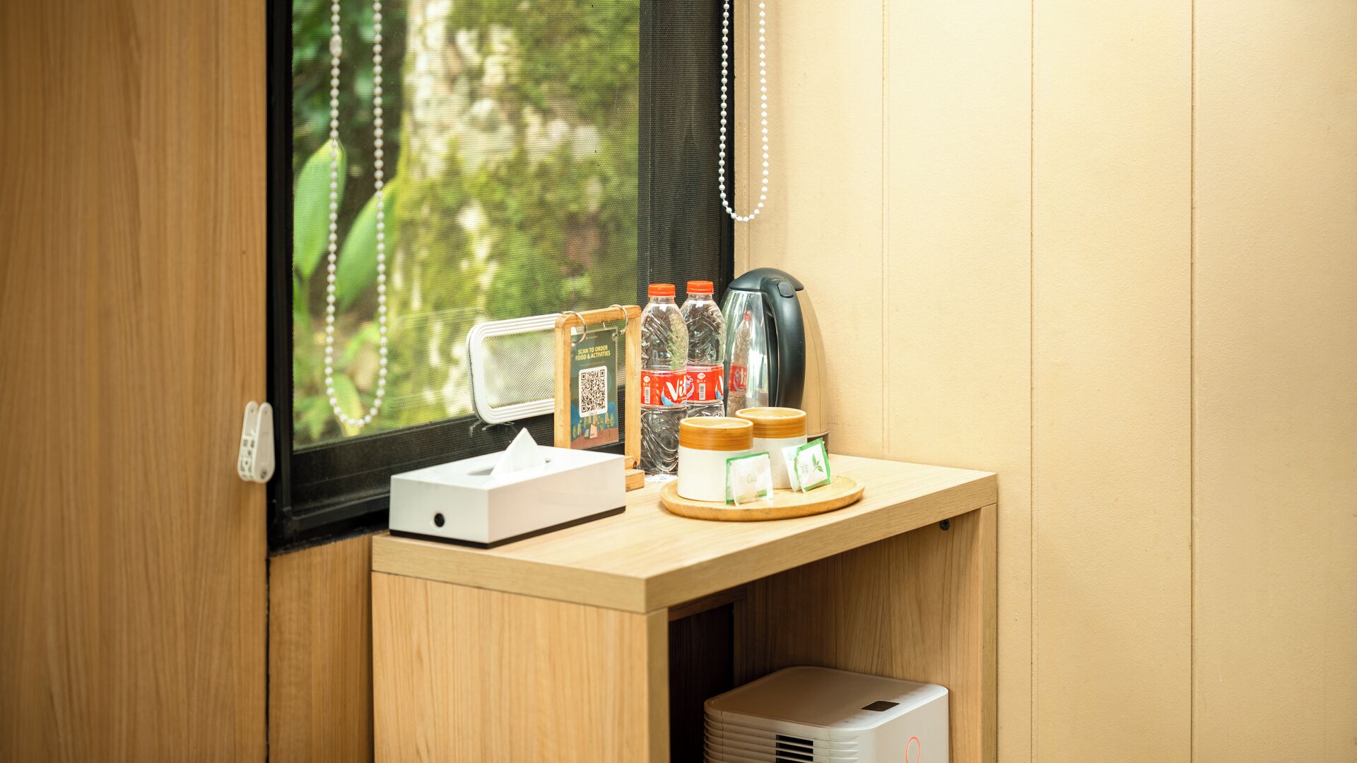 A wooden desk with a computer, two bottles of Vibe, a kettle, and a tissue box.