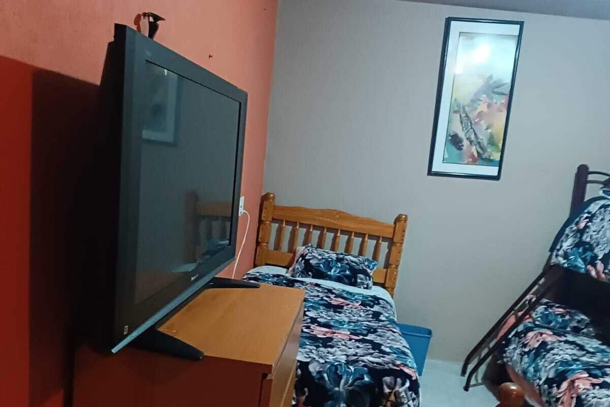 A bedroom with a bed, a wooden dresser, a television, and a framed picture on the wall.