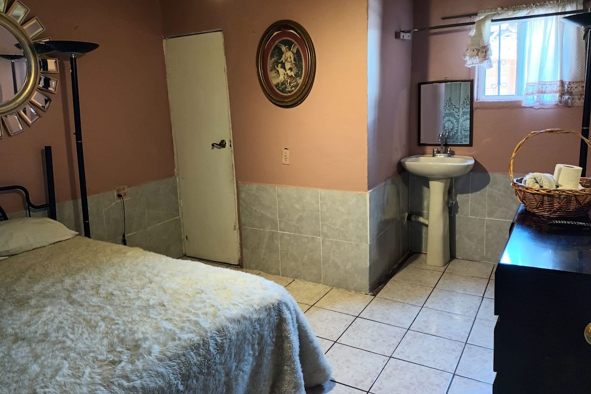 A room with a bed, a white door, a sink, a mirror, and a window with curtains.
