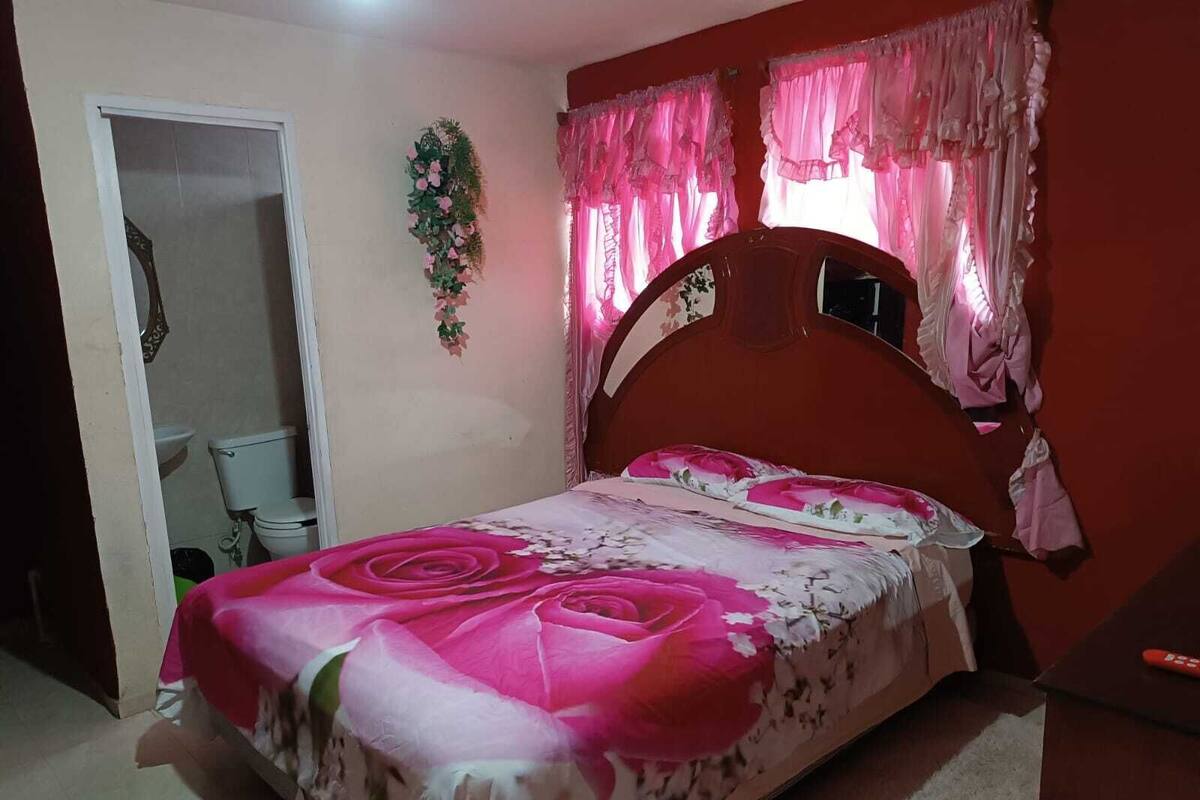 A bedroom with a bed, a door leading to a bathroom, and a window with curtains.