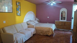 A bedroom with a bed, a white sofa, a ceiling fan, a dresser, and a mirror. - HOSPEDAJE BARATO MI CASITA DE COLORES (Tijuana)
