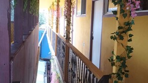 A narrow corridor with a yellow wall, a black metal railing, and pink flowers hanging from the railing. - HOSPEDAJE BARATO MI CASITA DE COLORES (Tijuana)
